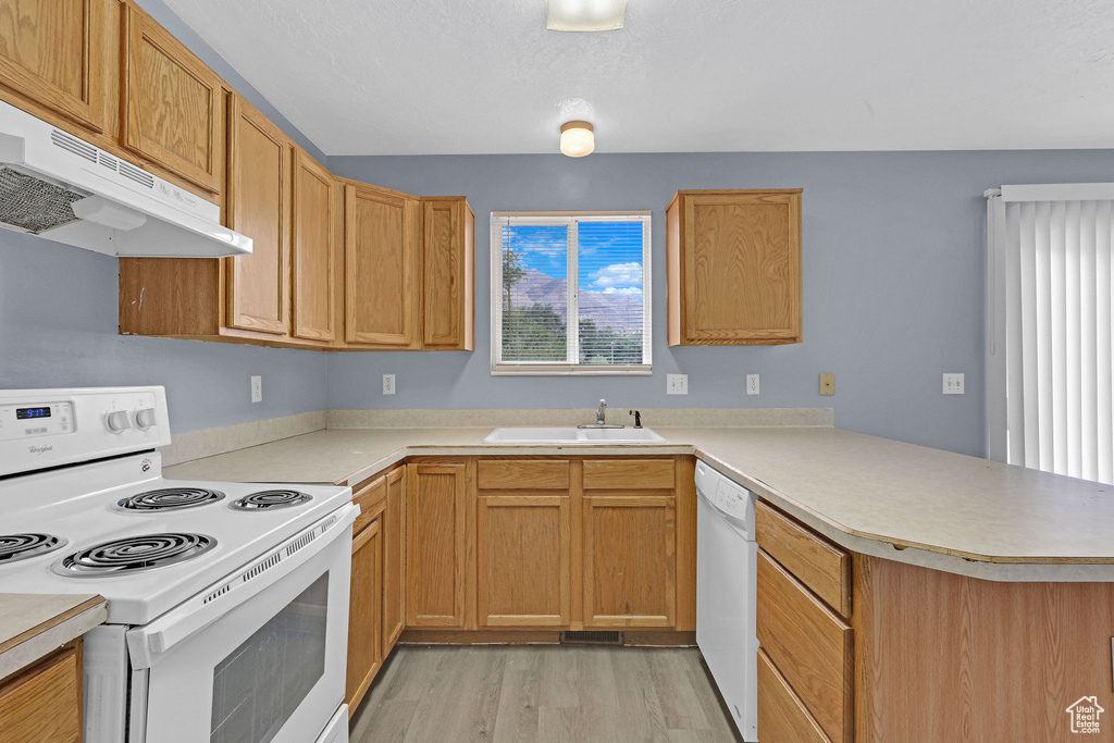 Kitchen featuring sink, light wood-type flooring, kitchen peninsula, and white appliances