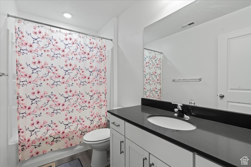 Full bathroom with vanity, toilet, hardwood / wood-style flooring, and shower / tub combo with curtain