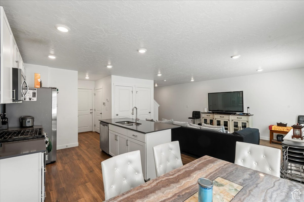 Kitchen featuring white cabinets, appliances with stainless steel finishes, a center island with sink, and dark hardwood / wood-style flooring