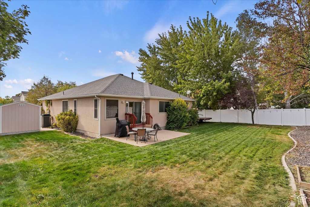 Back of property with a storage shed, a lawn, a patio area, and central AC