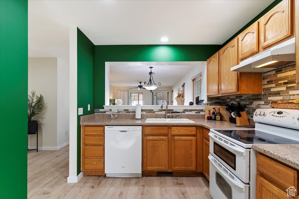 Kitchen with sink, white appliances, decorative light fixtures, backsplash, and light hardwood / wood-style floors