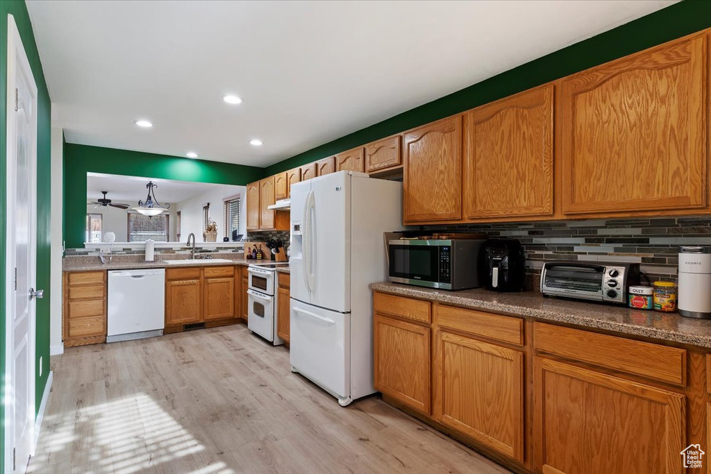 Kitchen with white appliances, backsplash, sink, and light wood-type flooring