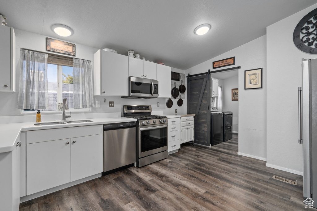 Kitchen with stainless steel appliances, white cabinets, washer and clothes dryer, sink, and a barn door