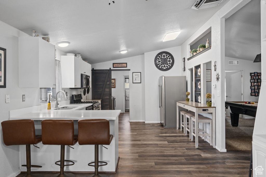 Kitchen with kitchen peninsula, appliances with stainless steel finishes, sink, and vaulted ceiling