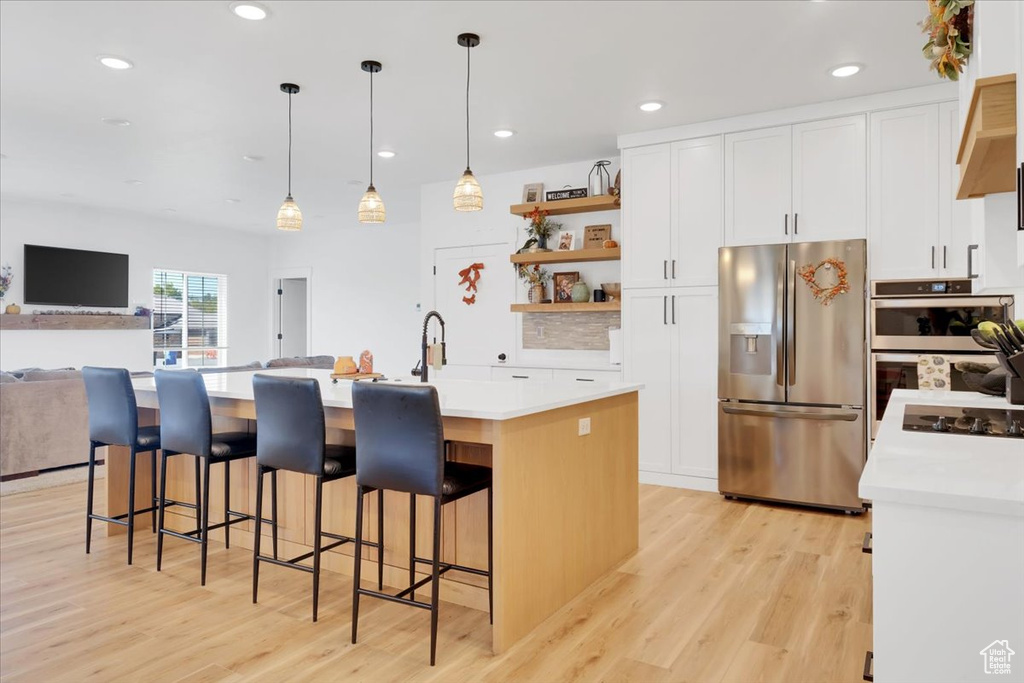 Kitchen featuring white cabinets, a kitchen island with sink, decorative light fixtures, appliances with stainless steel finishes, and light hardwood / wood-style floors