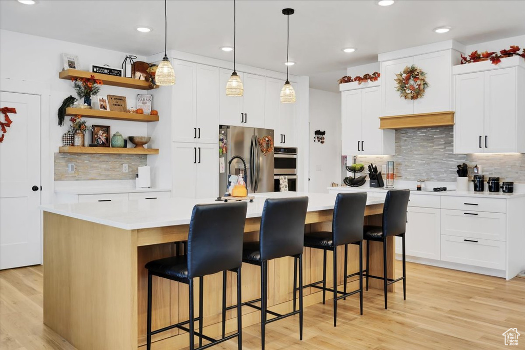 Kitchen with a kitchen island with sink, stainless steel appliances, and light wood-type flooring