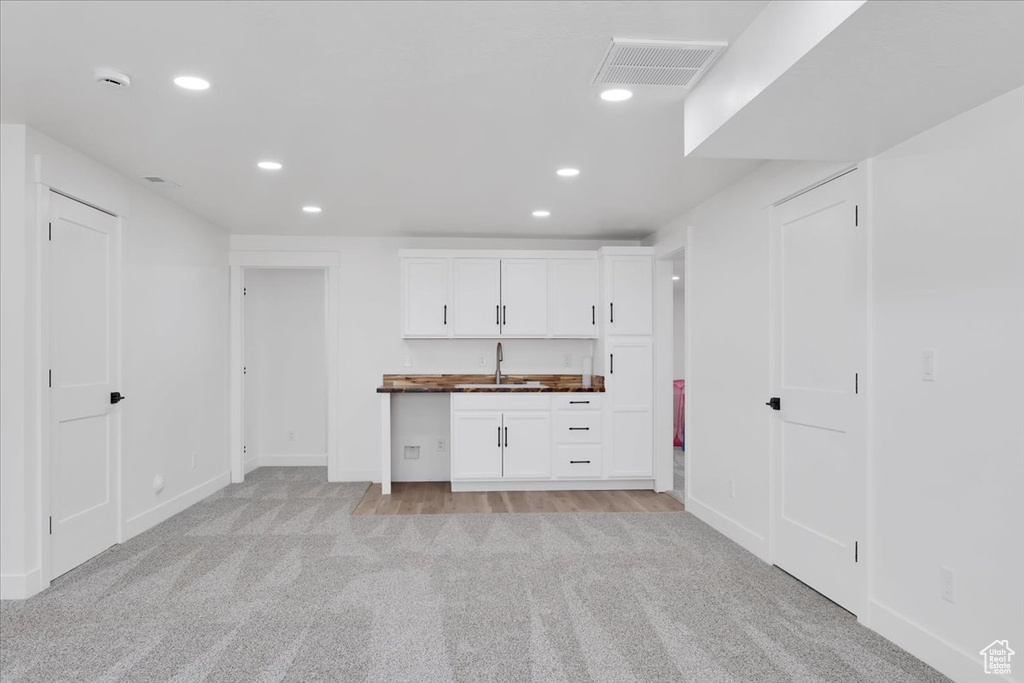 Interior space with white cabinetry, sink, and light colored carpet