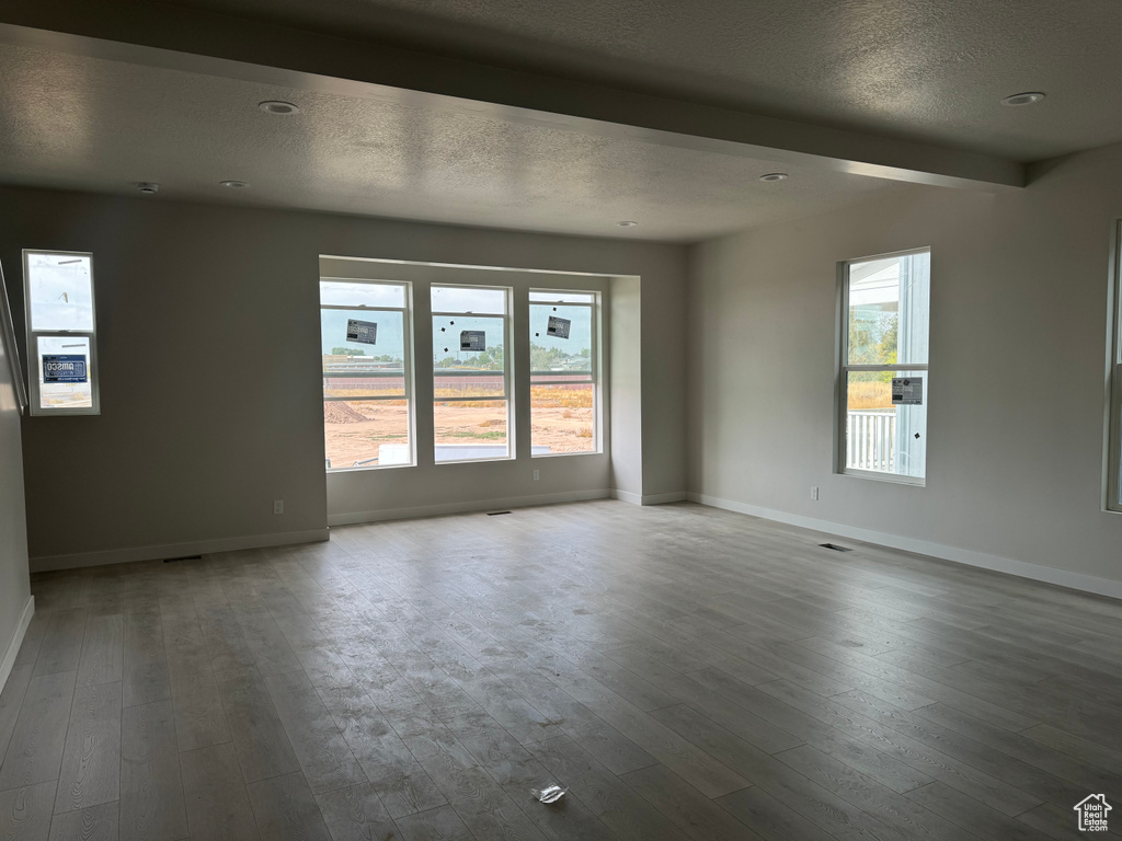 Unfurnished room with beam ceiling, hardwood / wood-style floors, and a textured ceiling