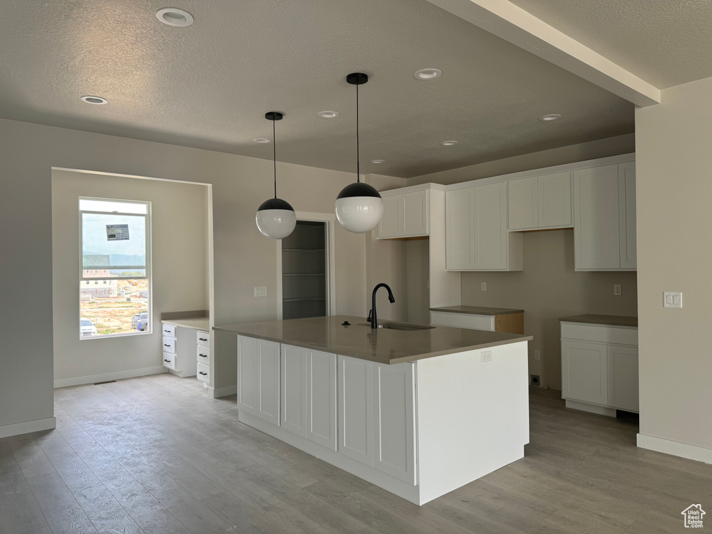 Kitchen featuring an island with sink, hanging light fixtures, sink, and white cabinetry