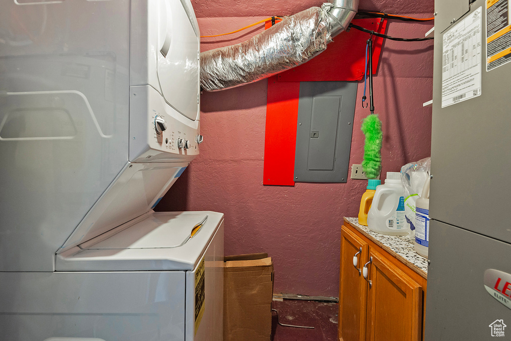 Laundry room with cabinets, electric panel, heating unit, and stacked washer / drying machine