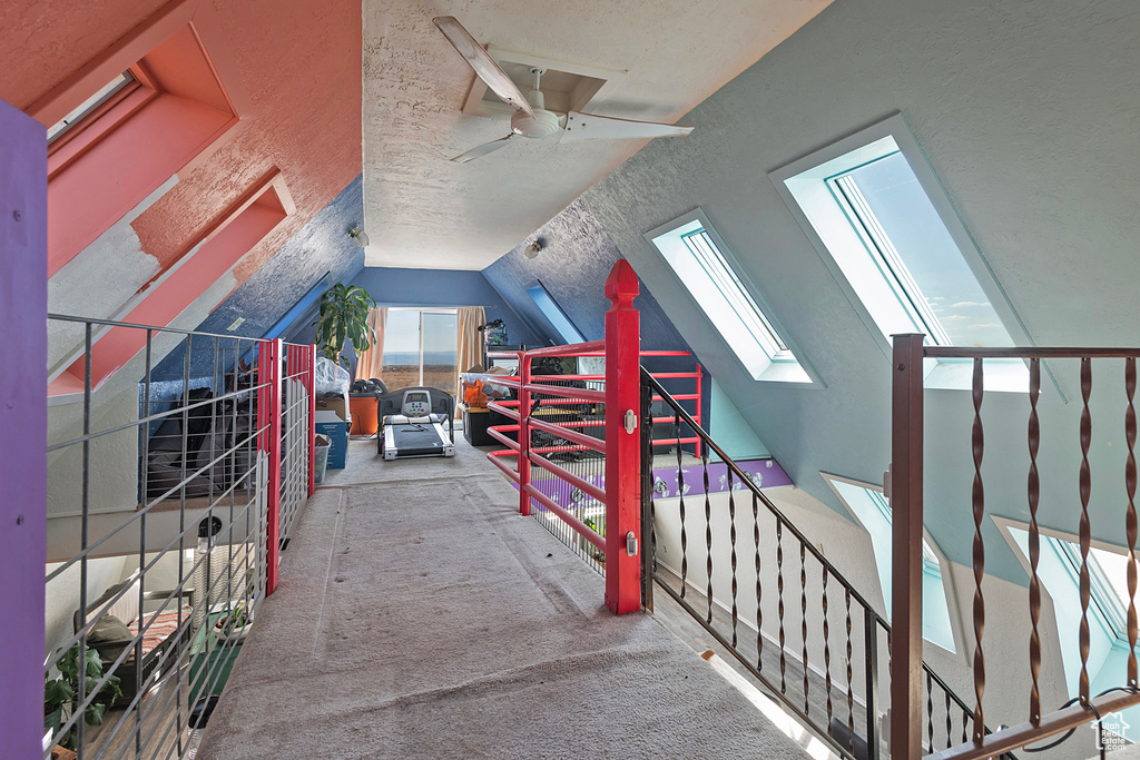 Additional living space with carpet flooring, ceiling fan, vaulted ceiling with skylight, and a textured ceiling