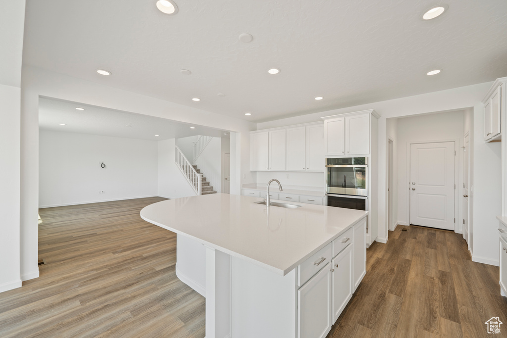 Kitchen with sink, stainless steel double oven, white cabinets, light hardwood / wood-style flooring, and a kitchen island with sink