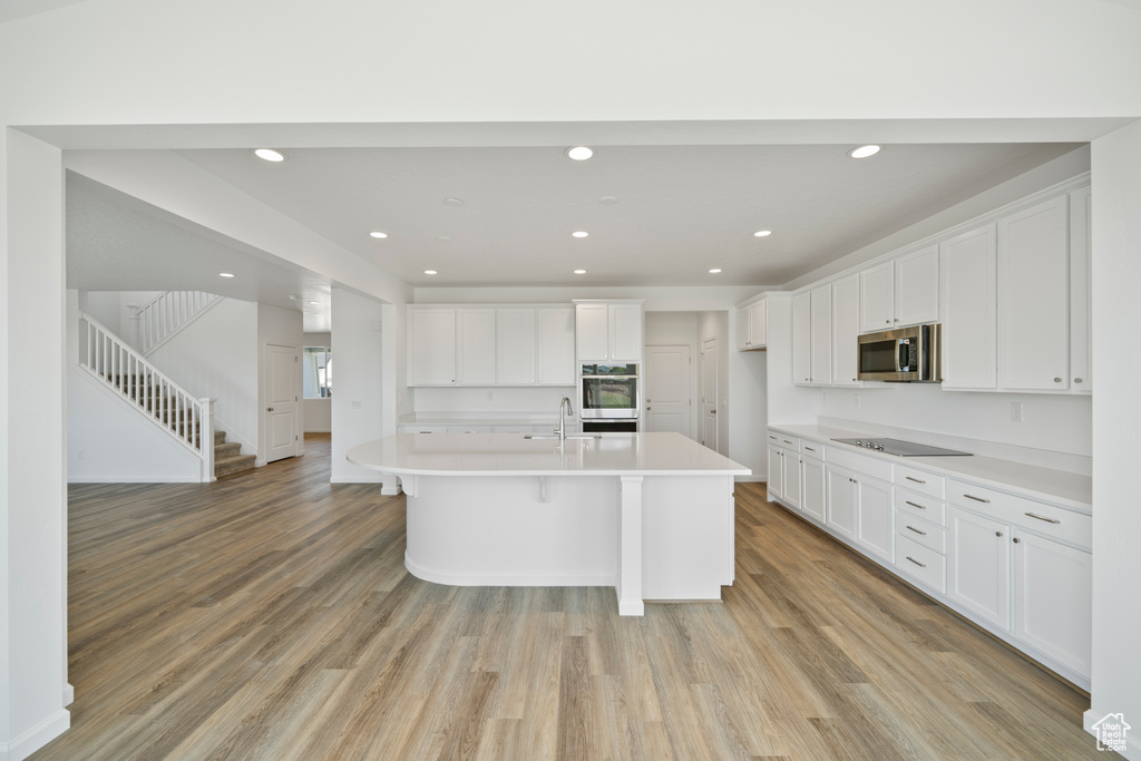 Kitchen with appliances with stainless steel finishes, light hardwood / wood-style flooring, white cabinets, and an island with sink