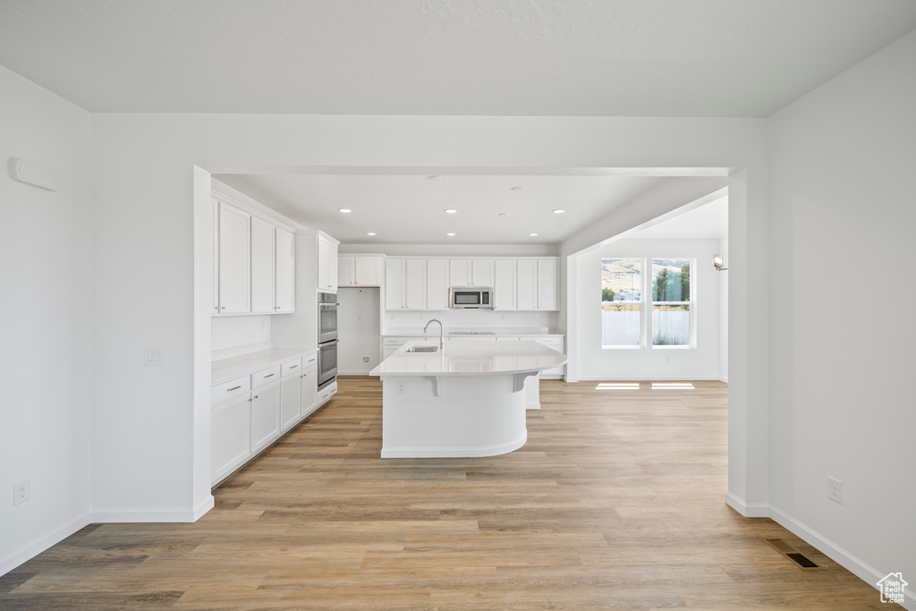 Kitchen featuring white cabinetry, appliances with stainless steel finishes, light wood-type flooring, and a center island with sink