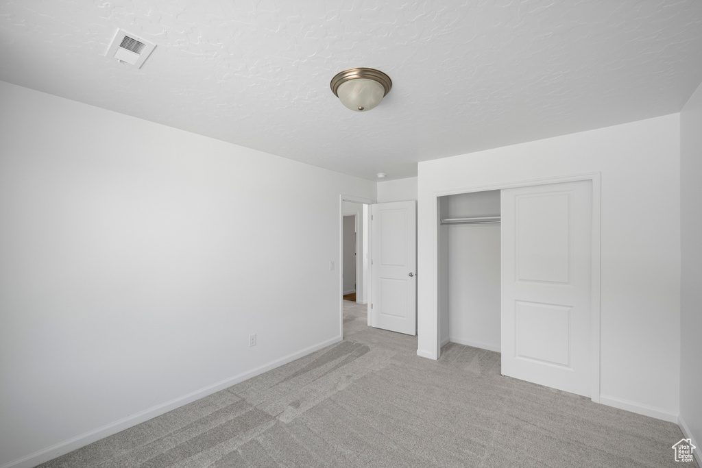 Unfurnished bedroom featuring a closet, light carpet, and a textured ceiling