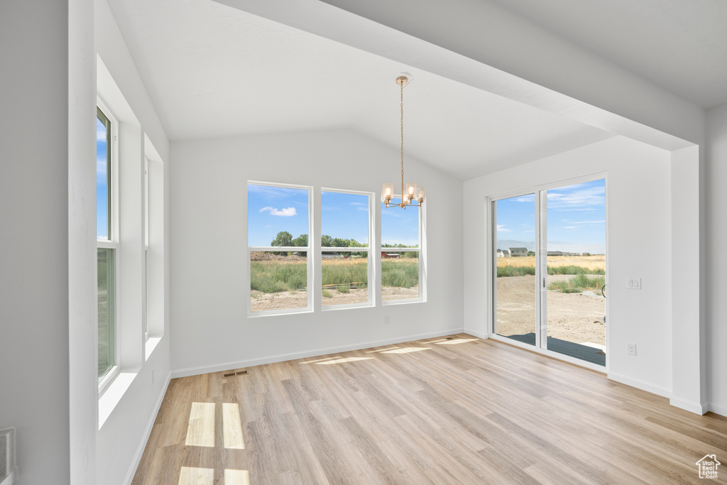 Unfurnished dining area featuring light hardwood / wood-style floors, vaulted ceiling, plenty of natural light, and an inviting chandelier