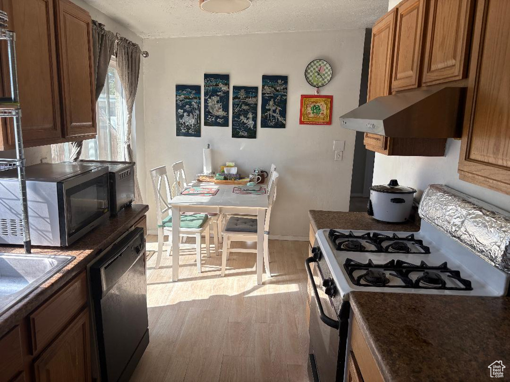 Kitchen with a textured ceiling, stainless steel appliances, light wood-type flooring, and range hood