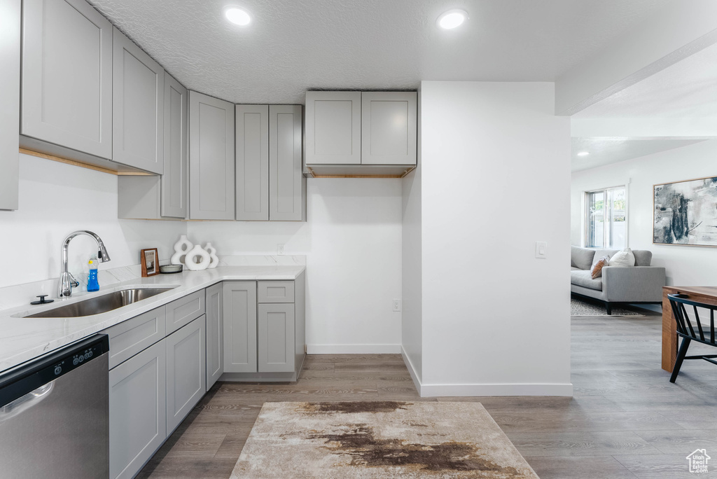 Kitchen with light hardwood / wood-style floors, gray cabinetry, sink, dishwasher, and a textured ceiling