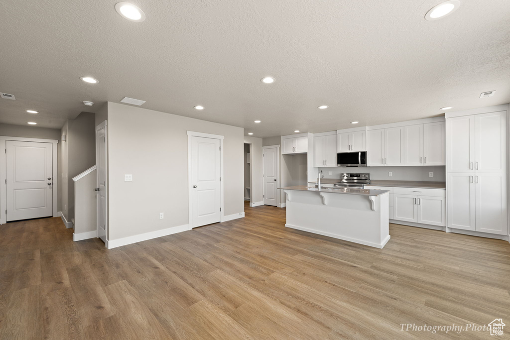 Kitchen with light hardwood / wood-style floors, white cabinetry, a center island with sink, stainless steel appliances, and a textured ceiling