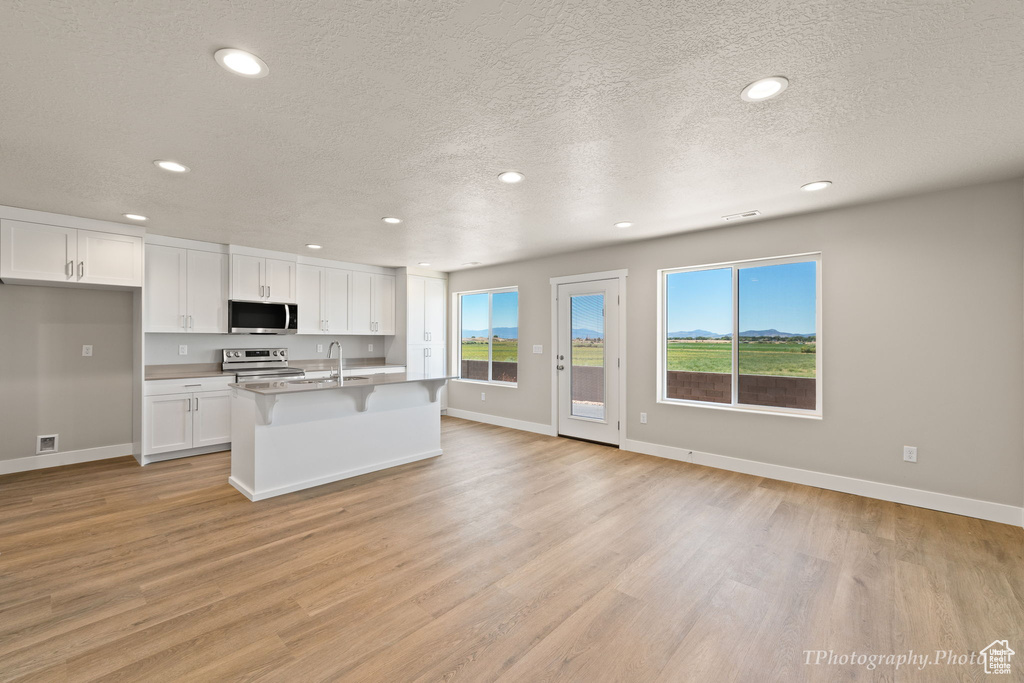 Kitchen featuring white cabinets, a textured ceiling, a center island with sink, light hardwood / wood-style flooring, and stainless steel appliances