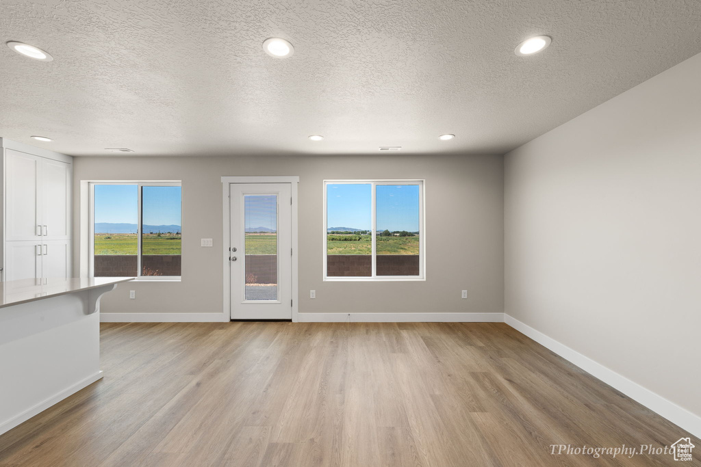 Unfurnished room featuring a textured ceiling, a healthy amount of sunlight, and light hardwood / wood-style flooring