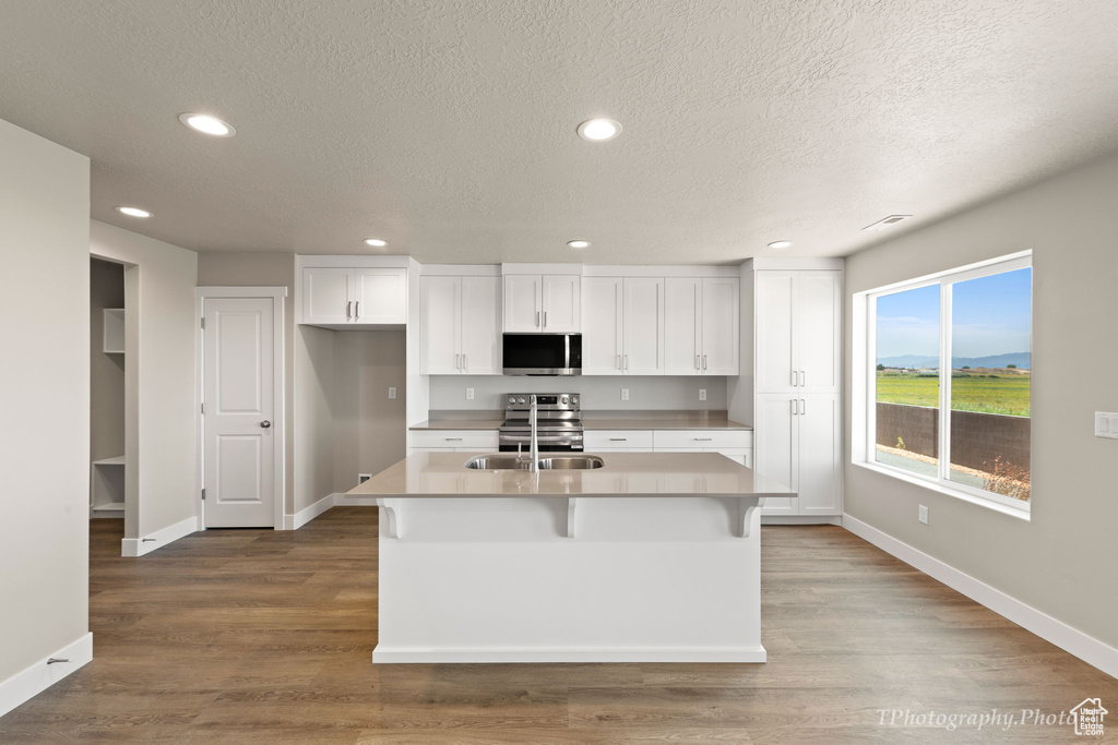 Kitchen featuring wood-type flooring, an island with sink, appliances with stainless steel finishes, and white cabinetry