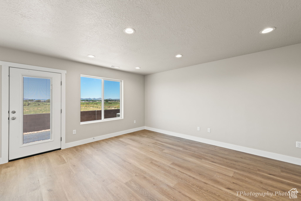 Empty room featuring light wood-type flooring and a textured ceiling