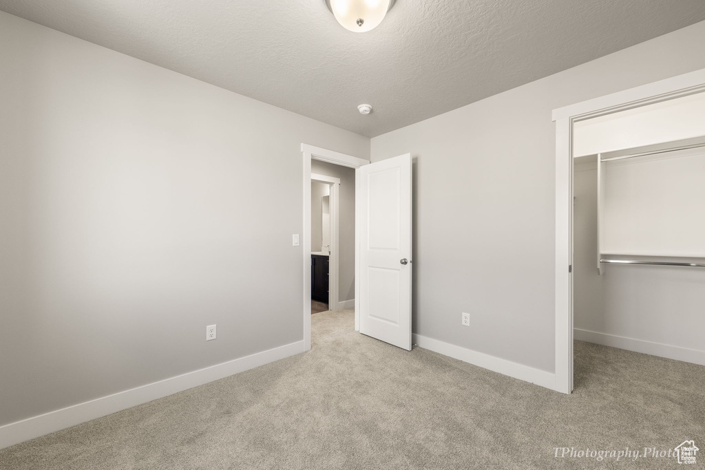 Unfurnished bedroom featuring light carpet, a textured ceiling, and a closet