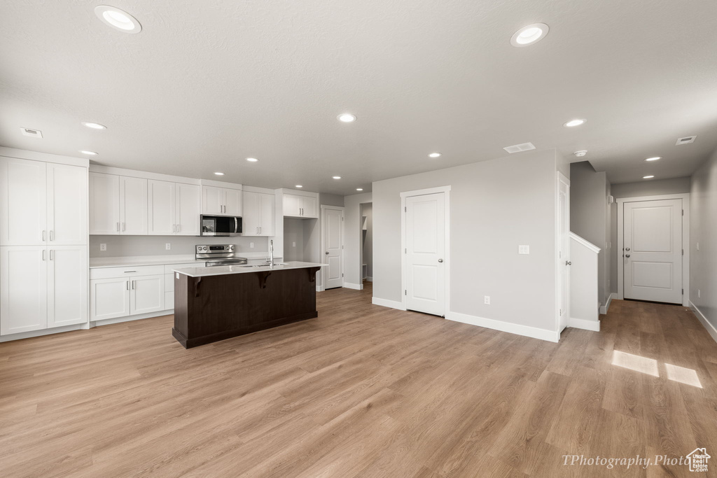 Kitchen with an island with sink, white cabinetry, appliances with stainless steel finishes, a breakfast bar, and light wood-type flooring