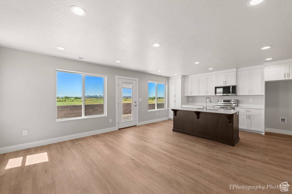 Kitchen featuring a kitchen island with sink, stainless steel appliances, sink, white cabinetry, and light hardwood / wood-style flooring