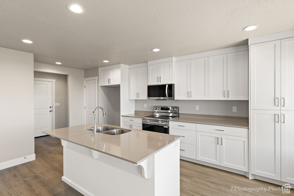 Kitchen with a kitchen island with sink, stainless steel appliances, and white cabinetry