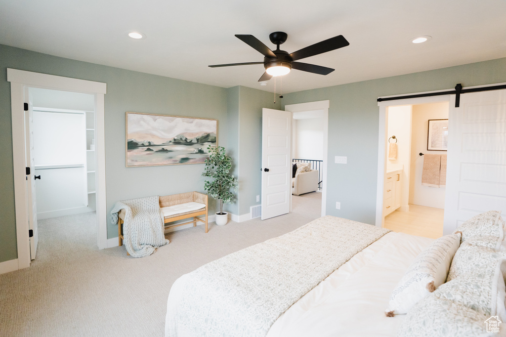 Bedroom featuring ceiling fan, ensuite bathroom, light carpet, and a barn door