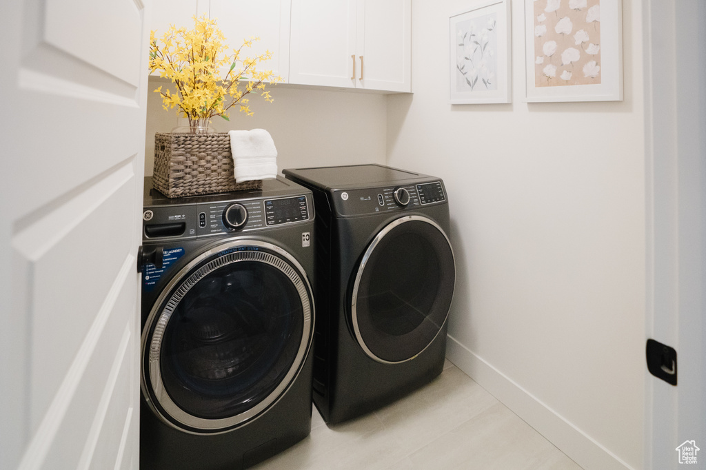 Clothes washing area featuring light tile patterned floors, cabinets, and washer and dryer