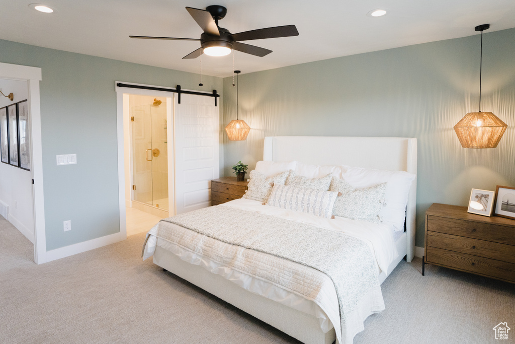 Carpeted bedroom featuring a barn door, connected bathroom, and ceiling fan