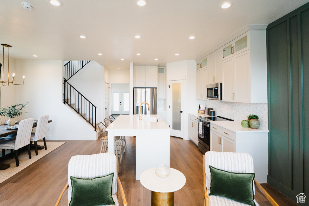 Kitchen with an island with sink, hardwood / wood-style floors, white cabinetry, appliances with stainless steel finishes, and decorative light fixtures