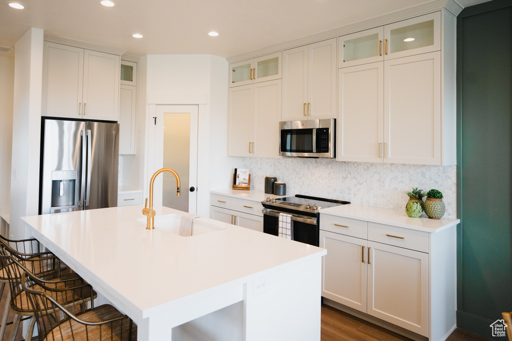 Kitchen featuring sink, a center island with sink, white cabinetry, stainless steel appliances, and a kitchen bar