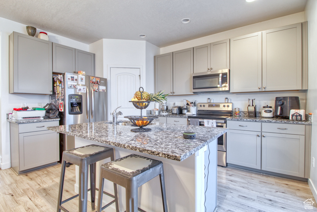 Kitchen featuring light stone counters, stainless steel appliances, light hardwood / wood-style flooring, a center island with sink, and gray cabinets