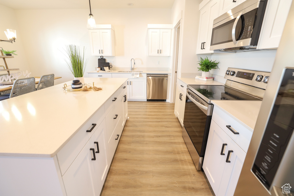 Kitchen with pendant lighting, sink, white cabinetry, appliances with stainless steel finishes, and light hardwood / wood-style floors