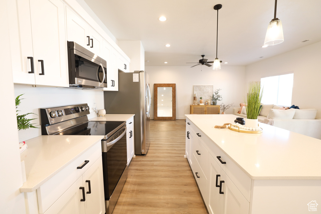 Kitchen with stainless steel appliances, pendant lighting, white cabinets, and light wood-type flooring