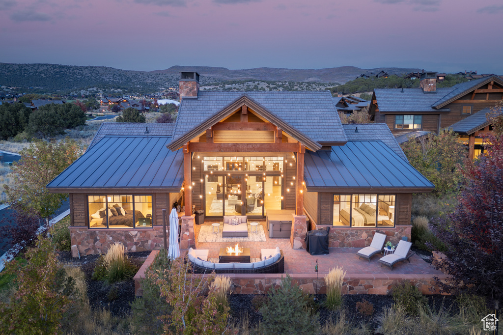 Back house at dusk with a mountain view, a multi sided fireplace, and a patio