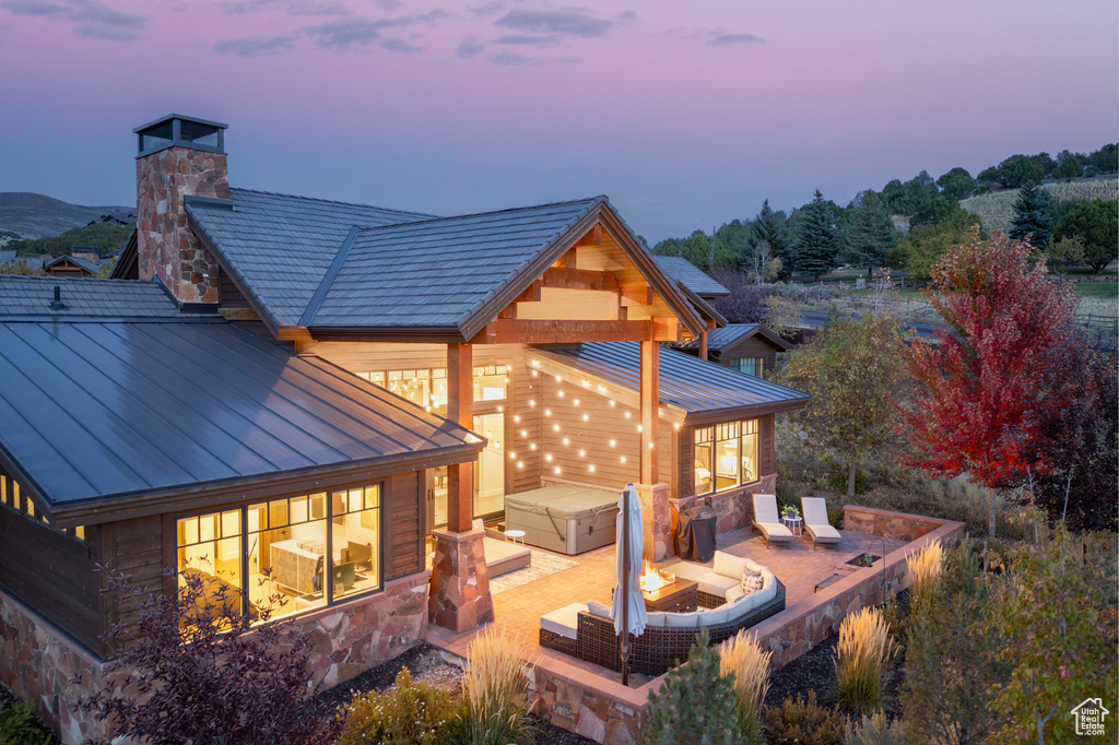 Back house at dusk featuring a jacuzzi and a patio