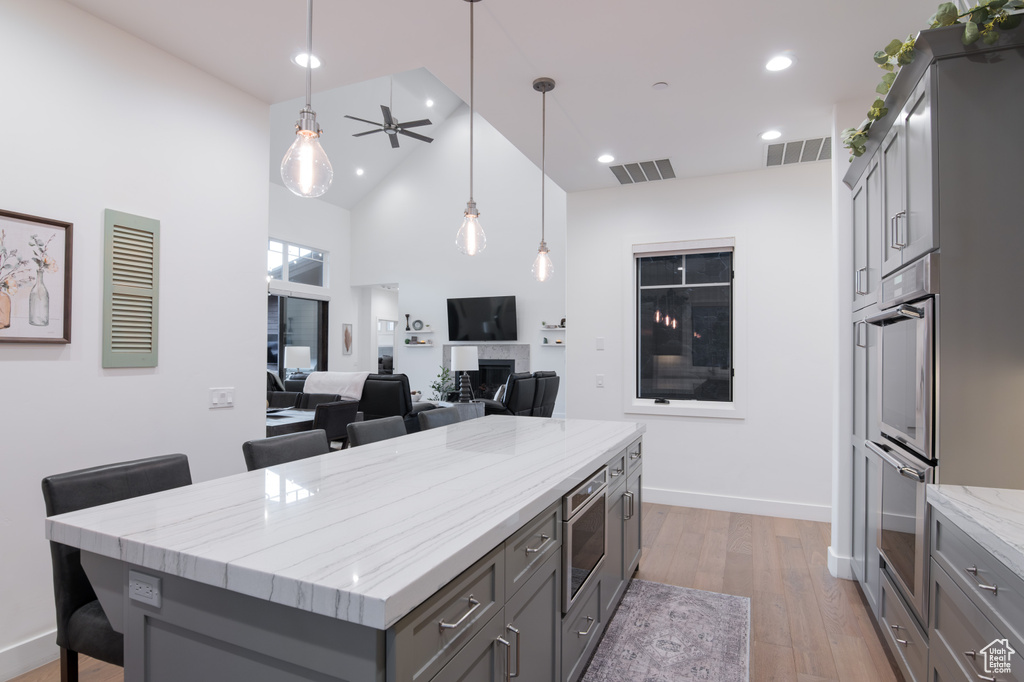 Kitchen featuring light hardwood / wood-style floors, gray cabinets, a kitchen island, light stone counters, and high vaulted ceiling