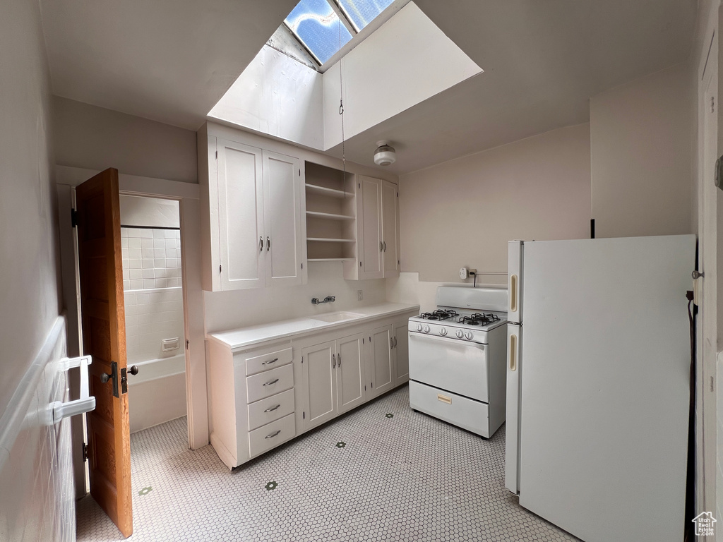 Kitchen featuring white cabinets, a skylight, sink, and white appliances