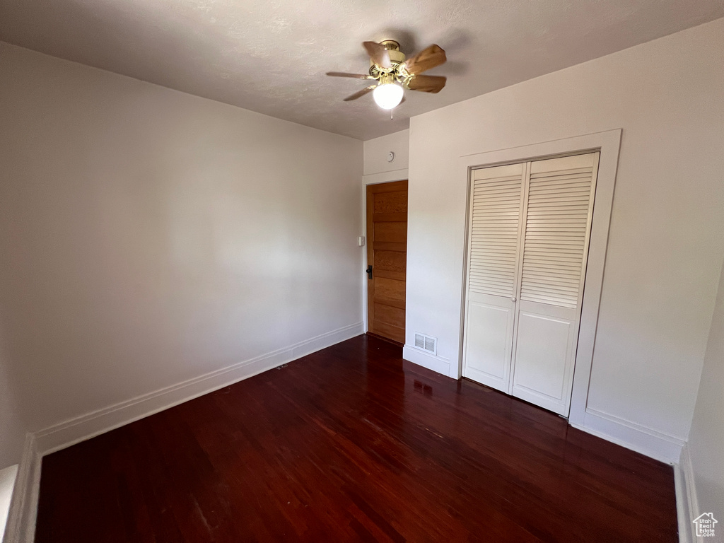 Unfurnished bedroom featuring a closet, dark hardwood / wood-style floors, and ceiling fan