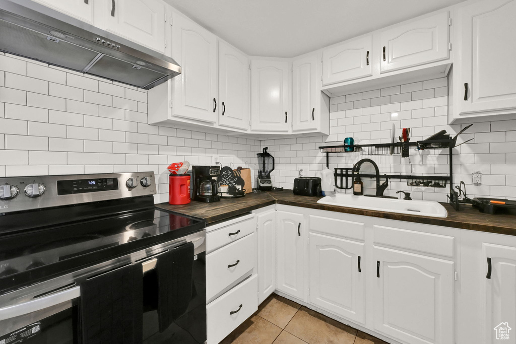 Kitchen with stainless steel electric stove, sink, wood counters, backsplash, and white cabinetry