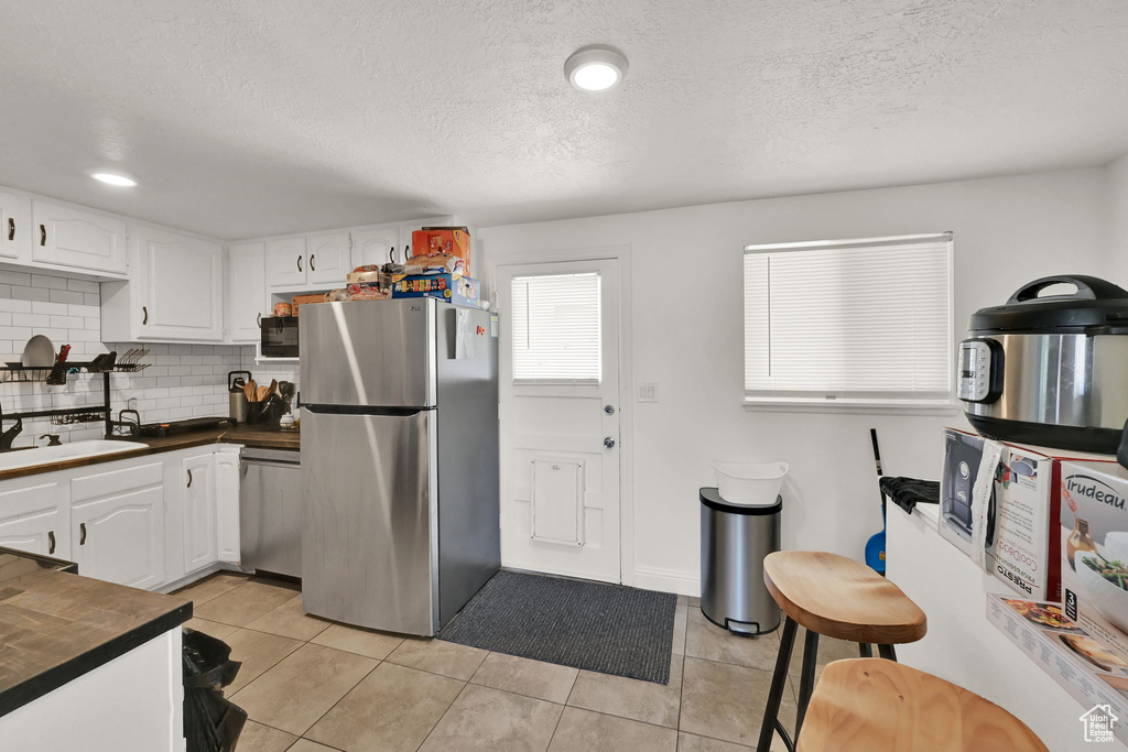 Kitchen with appliances with stainless steel finishes, white cabinetry, light tile patterned floors, and backsplash