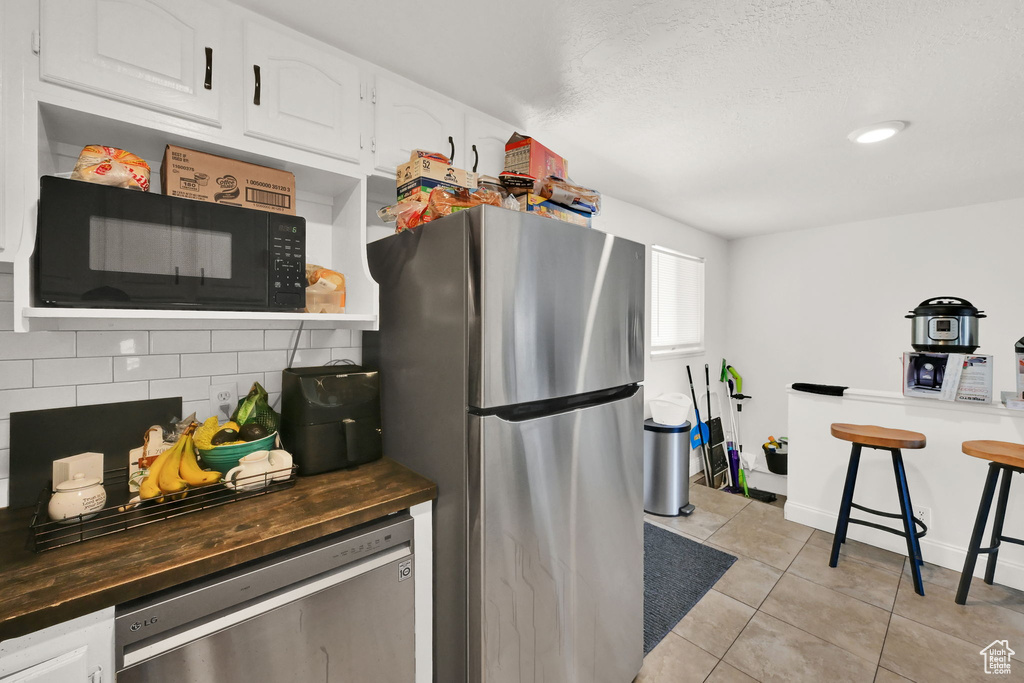 Kitchen featuring stainless steel appliances, decorative backsplash, light tile patterned floors, and white cabinetry