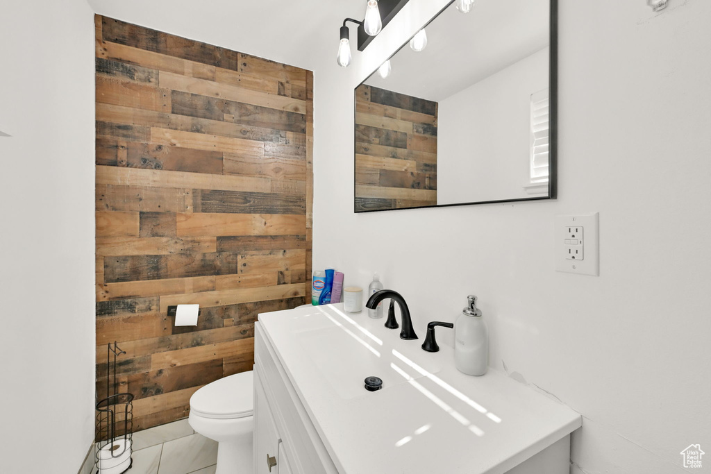 Bathroom featuring tile patterned flooring, vanity, wood walls, and toilet