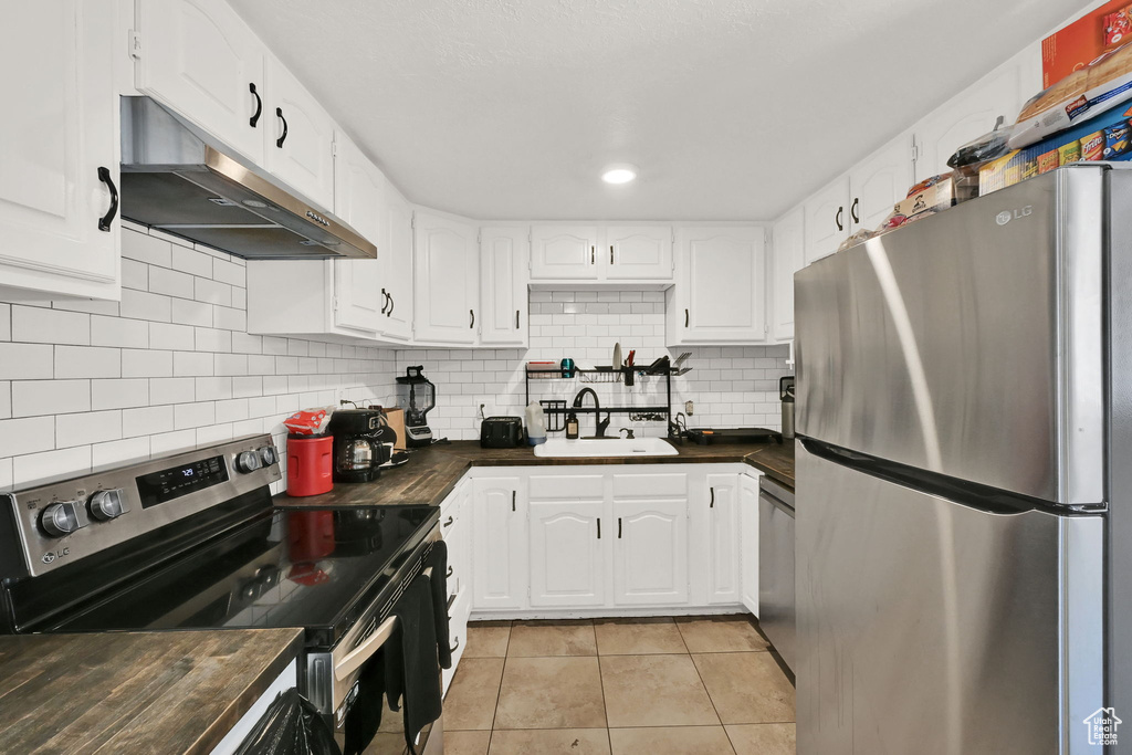 Kitchen featuring decorative backsplash, stainless steel appliances, white cabinets, sink, and butcher block countertops