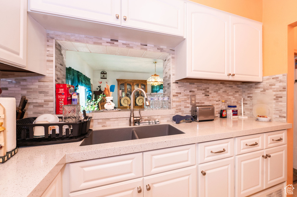 Kitchen featuring white cabinetry, hanging light fixtures, sink, and tasteful backsplash